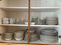 Shelves containing stacks of various white ceramic bowls, plates, a white teapot, and ramekins.