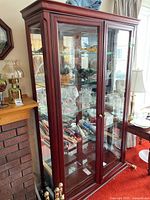 Front angled view of the wood framed glass display case with contents inside showing glass shelves and double glass front doors with brass knobs.