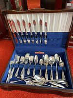 Full view of the open wooden flatware case showing organized knives, forks, spoons, and serving pieces in blue and white fabric lining.