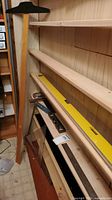 Wooden T-square, yellow 48" box level, smaller yellow level, tape measure, folding wooden ruler, steel ruler on shelves