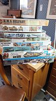 Seven stacked model kit boxes showing titles like H.M.S. Belfast, USS Arizona Battleship, Calypso, Vietnam Rescue, Missouri, Crab Offshore and US M113 ACAV tank.
