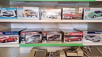 Ten boxed plastic car model kits in various scales. Mostly sealed. Images show box art with car models including Mustang, Camaro, Porsche, Corvette.