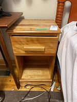 Front view of wood nightstand showing drawer and open storage area below, placed next to bed and table.