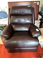 Front view showing brown leather upholstery with cushioned padded sections for back and armrests, visible scratches.
