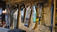 Photo of several hand saws hung on pegboard, including a metal handsaw, bow saw, hack saw, and work light in packaging.