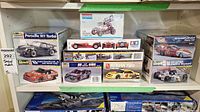 Shelf display with multiple sealed Revell model car kits including Porsche 911 Turbo, Dale Earnhardt Jr. 2001 Monte Carlo, McDonald's Firebird Funny Car, Castrol Reynard, and others.