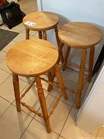 Three wooden stools with round seats and turned spindle legs, arranged on tiled floor