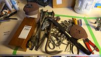 Photo showing assortment of metal hand tools, sanding discs, and accessories on a workbench with green tape borders.