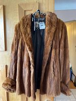 Full front view of the brown mink fur jacket hanging on a hanger showing front and black lining inside.