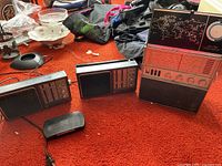 Two vintage GE solid state AM/FM/TV radios with tuning knobs, buttons, and frequency dials sitting on orange carpet among other household items.