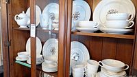 Full view of china service in wooden cabinet showing dinner plates, bowls, stacked cups and saucers, teapot, creamer, and sugar bowl