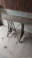 Full view of antique sewing table with iron lattice base and wooden top in an unfinished room.