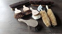 Seven assorted cleaning brushes on a wood surface, varying sizes and bristle types