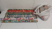 Multiple rolls of Christmas gift wrap paper lined up on the floor with various festive designs.