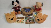 Full view of assorted Disney items including plush Mickey Mouse, plush Winnie the Pooh, Winnie the Pooh slippers, board game tin, and two children's storybooks with records.
