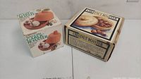 Photo of terra cotta garlic roaster box on left and chestnut roaster box on right, showing product packaging.