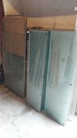 Glass shelves upright stacked against wall showing multiple flat sheets of glass mostly sized about 46 inches by 14 inches, dusty and needing cleaning