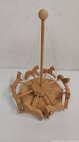 Front top-down angled view of the wooden carousel toy, showing the central pole, eight wooden horses, circular base, and attached strings.