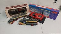 Grouped shot showing two vintage Hess trucks, one still in box, the Ferrari die-cast model, and the blue box for the RC car and model airplane kit.