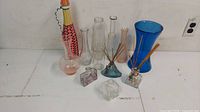 Overview of assorted glass items including multiple vases, incense holders with reed sticks, and a decorative wrapped bottle.