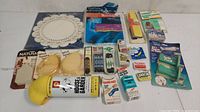 Overall lot includes vintage household items including shoe covers, adhesive shoe lifts, insect repellent spray, bandages, sewing kits, vacuum cleaner bags, and lace doilies.