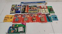 Top view of arranged vintage new old stock items including padlocks, adhesives, film, and tools on white surface