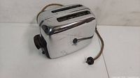 Full view of the vintage chrome Toastmaster toaster showing two wide slots for bread and original cloth power cord with plug.
