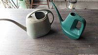 Two vintage plastic watering cans on a wooden surface, one beige and one green