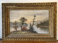 Front view of ornate gilt wood frame surrounding oil landscape painting on wooden surface