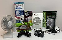 Grouped household items including fans, heater, irons, hair dryer, vacuum, cleaning supplies, and storage bag boxed and loose