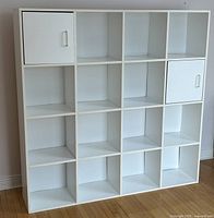 Front view of bookshelf showing 16 square cubby compartments with two cabinet doors on top left and middle right positions.