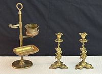 Photo of one brass toiletry bathroom caddy and two brass candle holders on black background.