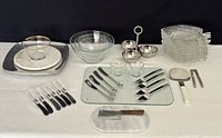 Full view of the lot items arranged on black backdrop showing tri-bowl dish, glass plates, spatulas, pate utensils, and other items.