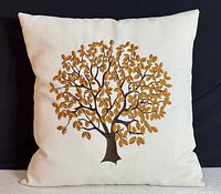 Full view of the cream colored cushion with an embroidered tree with golden-brown leaves and dark trunk and branches.