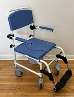 Front angle view of aluminium shower commode chair showing padded blue seat with opening and commode bucket underneath, armrests, wheels and footrests.