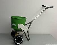 Side view of the green plastic drum garden spreader with metal frame and wheel.