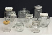 Nine assorted glass jars displayed on a surface with varied shapes and lids including glass, metal clasp, and wooden lids, showing overall variety in the lot.