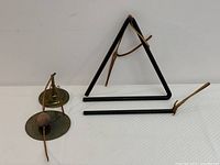 Front view of musical triangle with its striker and small brass gong with attached wooden striker on leather cord.
