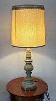 Full view of large table lamp lit, showing fabric shade and carved base on wooden table