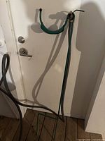 Full view of the green steel hose stand with attached hose and valve, leaning against a wall indoors