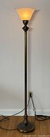 Full view of the entire metal floor lamp standing tall against a wall, plugged in, showing its height and sturdy base.