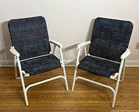 Front angled view of two folding patio chairs showing white aluminum frames and canvas covers with geometric pattern.