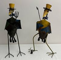 Pair of whimsical metal bird sculptures standing side by side with hats and props