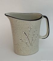 Side angled view showing the jug's speckled cream surface, dark rim, handle, and decorative branch pattern with raised dots.