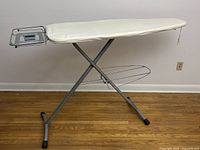 Side view showing full ironing surface with white double cover, metal frame, iron rest and shelf underneath