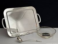 Photo showing large silver plated rectangular serving tray with handles, silver round wire basket style bowl and heavy ladle resting together