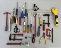Full assortment of hand tools laid out on a surface, showing all small tools including screwdrivers, clamps, paintbrush, scissors, pliers, hammer and rasp file.
