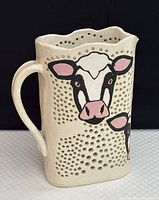 Front and side view of studio pottery milk jug showing cow face designs and dotted textured surface.
