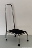 Sturdy metal foot stool with chrome legs and black rubber platform, showing side angle and handle height.