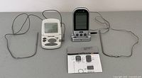 Two digital meat thermometers with wired metal probes on table with instruction manual visible.